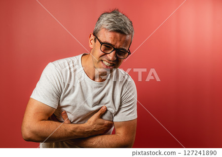 Man experiencing discomfort while holding his chest Man experiencing discomfort while holding his chest 127241890