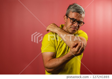 Man examining his arm for discomfort against a colored backdrop 127241893