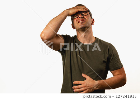 Man holds his stomach in discomfort while standing indoors Man holds his stomach in discomfort while standing indoors 127241913