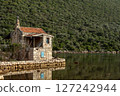 An old stone house stands still by the water, wrapped in the silence of green hills. 127242944