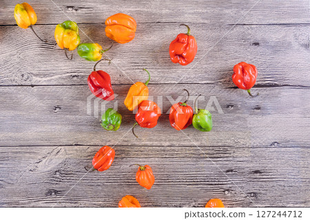 Various habanero peppers in bright colors scattered on wooden surface create an appetizing display. Various habanero peppers in bright colors scattered on wooden surface create an appetizing display. 127244712