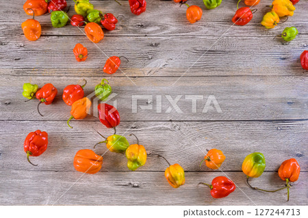 Fresh habanero peppers in various colors are scattered on weathered wooden table, showcasing their vibrant appearance. 127244713