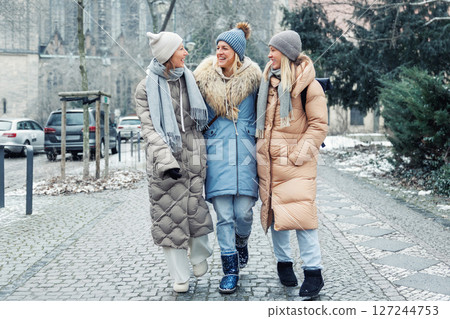 Three cheerful young adult women friend walk Magdeburg street old european uk german town city street enjoy having fun laughing cold winter day together. Female persons friendship celebration weekend 127244753