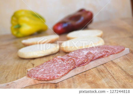 Sliced Salami and Fresh Buns on a Wooden Board with Green Onions 127244818