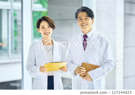 Male and female doctors in lab coats meeting in the hospital corridor Male and female doctors in lab coats meeting in the hospital corridor 127244825