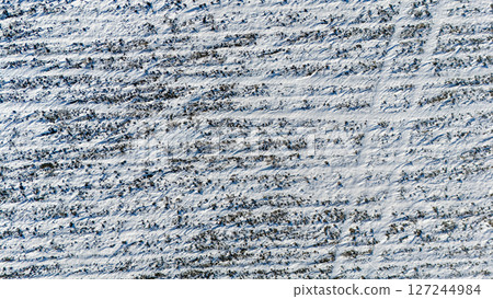 Drone view over a snow covered agriculture field with cultivated rows from crops. Drone view over a snow covered agriculture field with cultivated rows from crops. 127244984