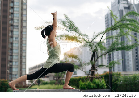 Asian woman 30s fitness yoga workout and stretching exercise reduces medical injury risk like shoulder pain muscle strain or inflammation for wellness healthcare urban city sunset, healthy 127245139