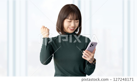 一位年輕女性/女商人正看著她的智慧型手機，並握拳 127248171