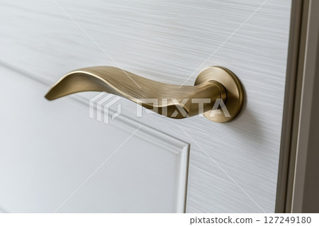 Golden Doorknob. Metal door handle lock and latch of brass on veneer doors. Copper door handle. White door wooden half opening through interior background. Modern trends in interior design. Close-up. 127249180