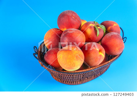 Woven basket overflows with fresh peaches, showcasing their rich colors natural beauty on blue background. Woven basket overflows with fresh peaches, showcasing their rich colors natural beauty on blue background. 127249403