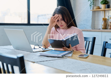 Middle aged sad stressed woman sitting at home office at table with computer Middle aged sad stressed woman sitting at home office at table with computer 127249811