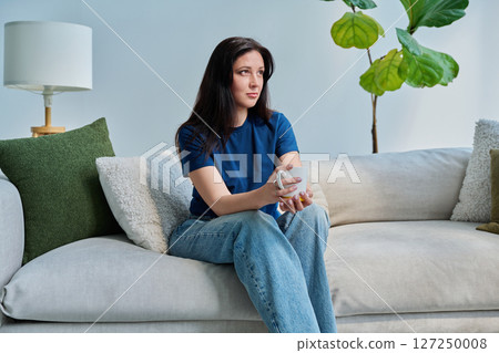 Portrait of beautiful smiling young brunette woman sitting on sofa in living room 127250008