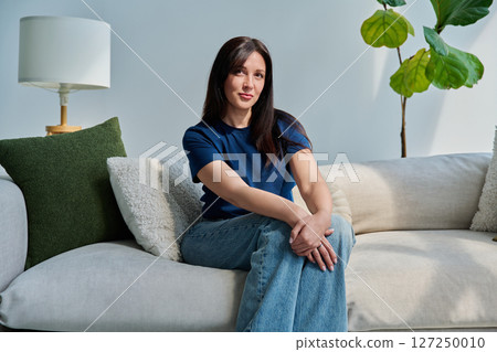 Portrait of beautiful young brunette woman sitting on sofa in living room Portrait of beautiful young brunette woman sitting on sofa in living room 127250010