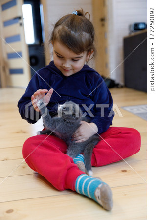 A Young Child Interacts Tenderly with a Playful Gray Kitten in a Cozy Indoor Environment, Sharing a Joyous Moment Full of Laughter and Connection on a Wooden Floor A Young Child Interacts Tenderly with a Playful Gray Kitten in a Cozy Indoor Environment, Sharing a Joyous Moment Full of Laughter and Connection on a Wooden Floor 127250092