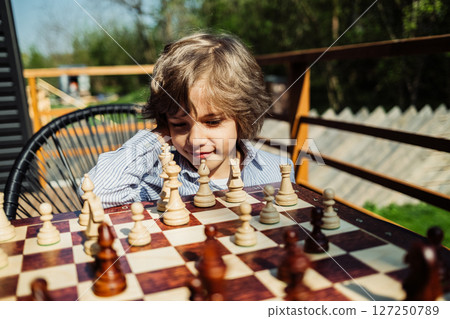 Schoolboy playing board game - wooden chess. Little boy child moves a pawn piece 127250789