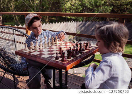 Little boys friends playing board game - chess. Children learning to move pieces Little boys friends playing board game - chess. Children learning to move pieces 127250793