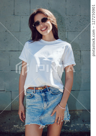 Young Woman In A White T-Shirt And Denim Skirt Posing Against Concrete Wall Young Woman In A White T-Shirt And Denim Skirt Posing Against Concrete Wall 127250901