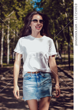 Happy Young Woman In White T-Shirt And Denim Skirt Walking In Park Happy Young Woman In White T-Shirt And Denim Skirt Walking In Park 127250919
