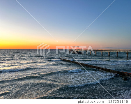 Golden sunset over calm sea with wooden pier stretching into water. Meditation content, moody aesthetics. 127251146