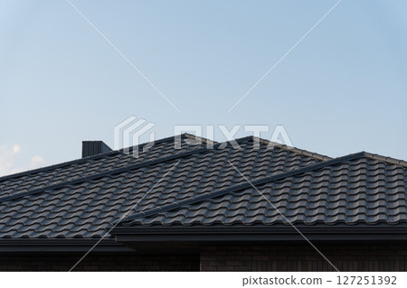Dark tiled roofs rise against a pale blue sky, showcasing modern architecture in a peaceful suburban setting during late afternoon 127251392