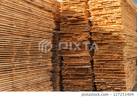 Tall stacks of neatly arranged timber await further processing in a bright and spacious wood processing facility Tall stacks of neatly arranged timber await further processing in a bright and spacious wood processing facility 127251404
