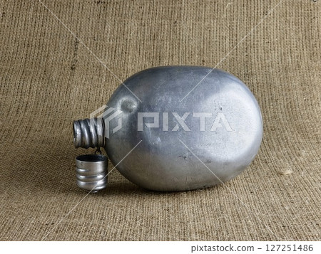 An old soldier's aluminum flask on a burlap. A thermos for water. An empty flask with an unscrewed cap. 127251486