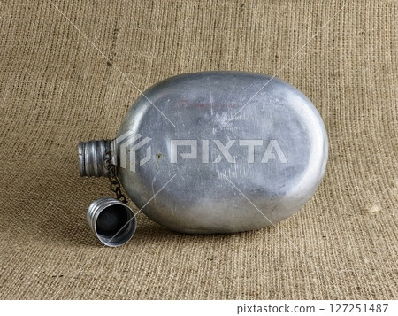 Old soldier's aluminum flask on burlap. A thermos for water. An empty flask with an unscrewed cap. 127251487