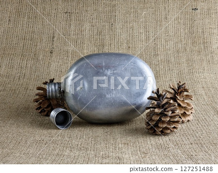 Old soldier's aluminum canteen with a lid on a chain on burlap. Thermos for water. Empty canteen with an unscrewed stopper. 127251488