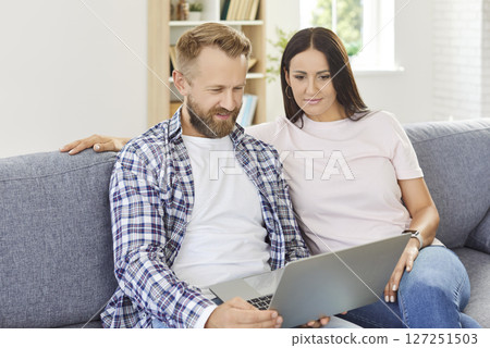 Young couple sitting on sofa at home using laptop for social media watching news or funny video. Young couple sitting on sofa at home using laptop for social media watching news or funny video. 127251503