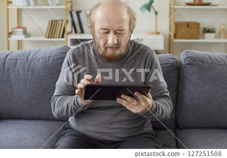Bearded senior man trying to understand how to use modern technologies, holding digital tablet 127251508