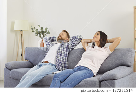 Smiling young family couple relaxing on couch, resting and enjoying peaceful break at home together. Smiling young family couple relaxing on couch, resting and enjoying peaceful break at home together. 127251514