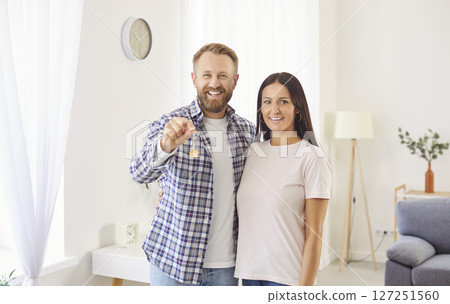 Happy young couple showing keys to camera, husband and wife excited by moving into new modern flat Happy young couple showing keys to camera, husband and wife excited by moving into new modern flat 127251560