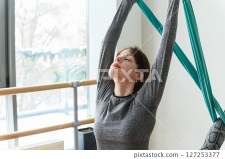 Focused woman doing aerial yoga stretch on teal silks. 127253377