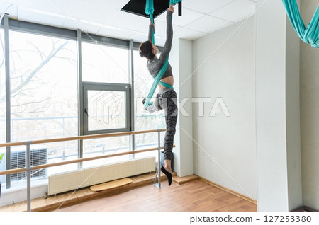 Woman performing aerial silks acrobatics in bright dance studio. 127253380