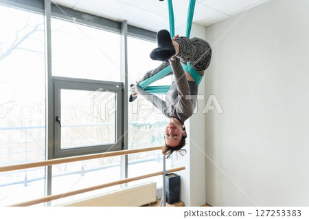 Athletic woman performing an inverted pose on teal aerial silks. Athletic woman performing an inverted pose on teal aerial silks. 127253383