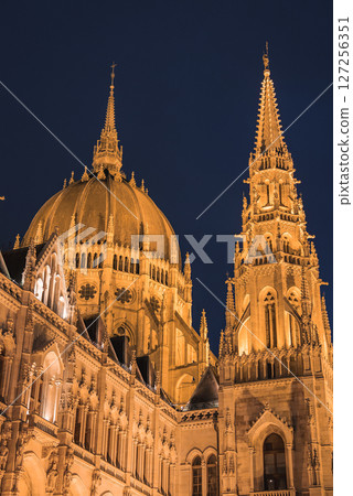 The neo Gothic Hungarian Parliament Building in Budapest is lit at night, showcasing its grand dome, intricate spires, and ornate architectural details. 127256351
