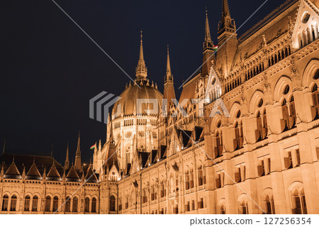 The Hungarian Parliament Building in Budapest glows at night, showcasing neo Gothic architecture with spires, a central dome, and intricate details. 127256354