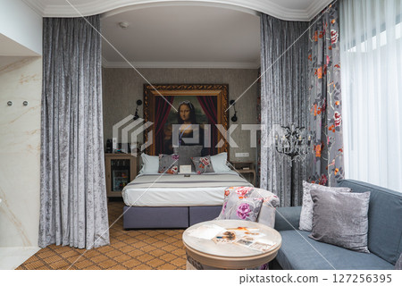 Elegant hotel room featuring a plush bed, modernized Mona Lisa portrait, gray velvet curtains, floral accents, and marble details for a cozy ambiance. 127256395