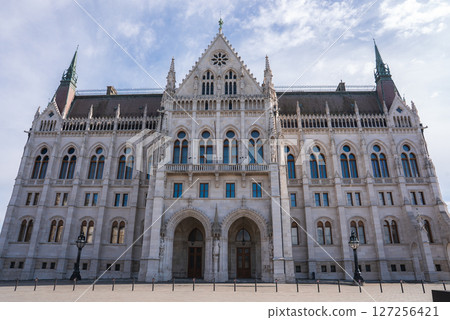 The Hungarian Parliament Building in Budapest displays a symmetrical facade with pointed arches, tall spires, and intricate stonework under a clear blue sky. The Hungarian Parliament Building in Budapest displays a symmetrical facade with pointed arches, tall spires, and intricate stonework under a clear blue sky. 127256421