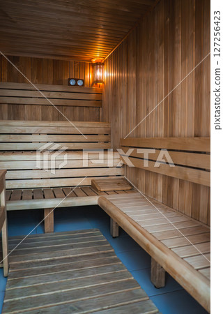 Wooden sauna interior with tiered benches, warm ambient lighting, a wooden mat on the floor, and functional dials on the back wall. 127256423