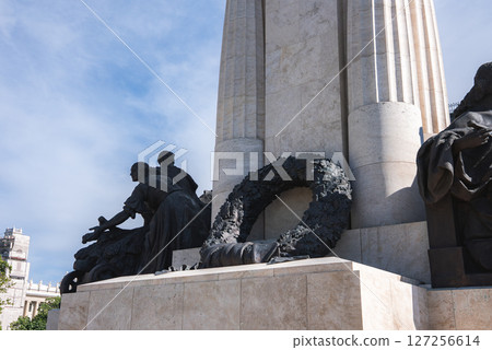 A tall stone column with intricate sculptures at its base, including human figures and a wreath, set against a bright blue sky in Budapest, Hungary. A tall stone column with intricate sculptures at its base, including human figures and a wreath, set against a bright blue sky in Budapest, Hungary. 127256614