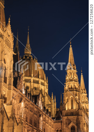 The neo Gothic Hungarian Parliament Building in Budapest glows with golden light, showcasing its dome, spires, and intricate carvings at dusk. 127256620
