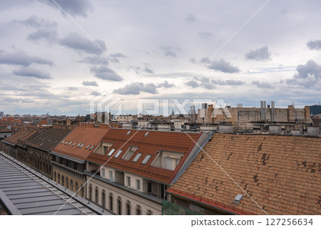 Rooftop view of Budapest, Hungary, showing red tiled and flat roofs, distant spires, and chimneys under a cloudy sky, highlighting urban architecture. Rooftop view of Budapest, Hungary, showing red tiled and flat roofs, distant spires, and chimneys under a cloudy sky, highlighting urban architecture. 127256634