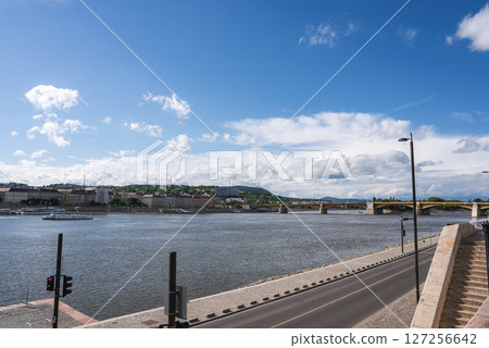 The Danube River flows through Budapest, Hungary, with a bridge in the background, buildings on the left, and a road with a staircase in the foreground. The Danube River flows through Budapest, Hungary, with a bridge in the background, buildings on the left, and a road with a staircase in the foreground. 127256642
