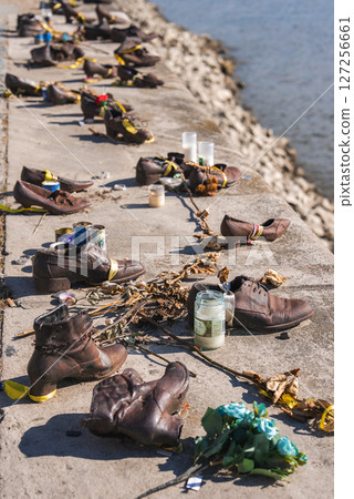 Bronze shoes line the riverbank in Budapest, Hungary, honoring Holocaust victims. Candles, flowers, and offerings are placed near the serene Danube River. 127256661