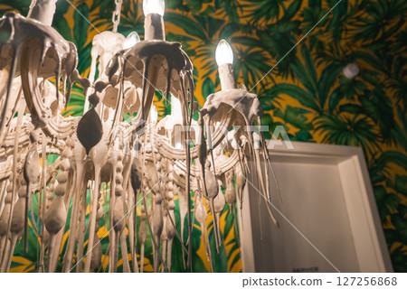 A unique chandelier with a melted wax like design and exposed bulbs, set against vibrant green and yellow tropical themed wallpaper with a white door. A unique chandelier with a melted wax like design and exposed bulbs, set against vibrant green and yellow tropical themed wallpaper with a white door. 127256868