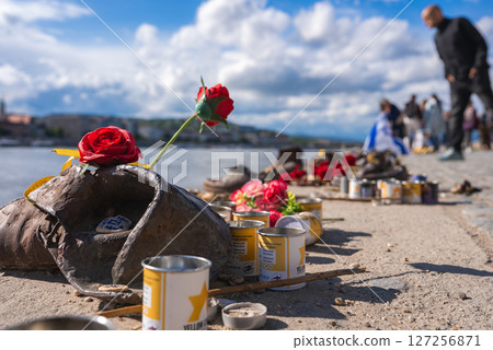 The Shoes on the Danube Bank memorial in Budapest features rusted iron shoes adorned with red roses and candles, with the Danube River in the background. The Shoes on the Danube Bank memorial in Budapest features rusted iron shoes adorned with red roses and candles, with the Danube River in the background. 127256871