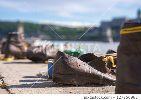 Bronze shoes line the Danube River in Budapest, Hungary, honoring Holocaust victims. The Chain Bridge and Buda Castle appear in the background. 127256968