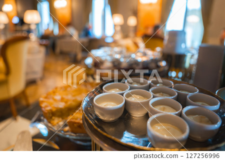 Interior of a boutique hotel dining area with soft lighting, plush seating, and a tray of creamy desserts and pastries in the foreground. 127256996