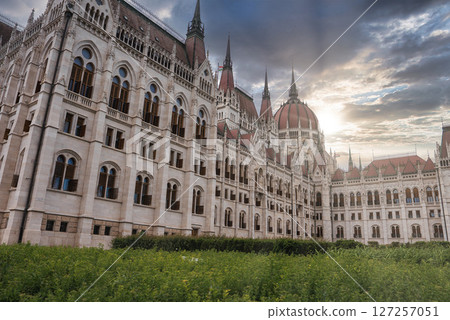 The Hungarian Parliament Building in Budapest is shown with its red dome, spires, and intricate details, framed by sunlight and a green foreground. The Hungarian Parliament Building in Budapest is shown with its red dome, spires, and intricate details, framed by sunlight and a green foreground. 127257051
